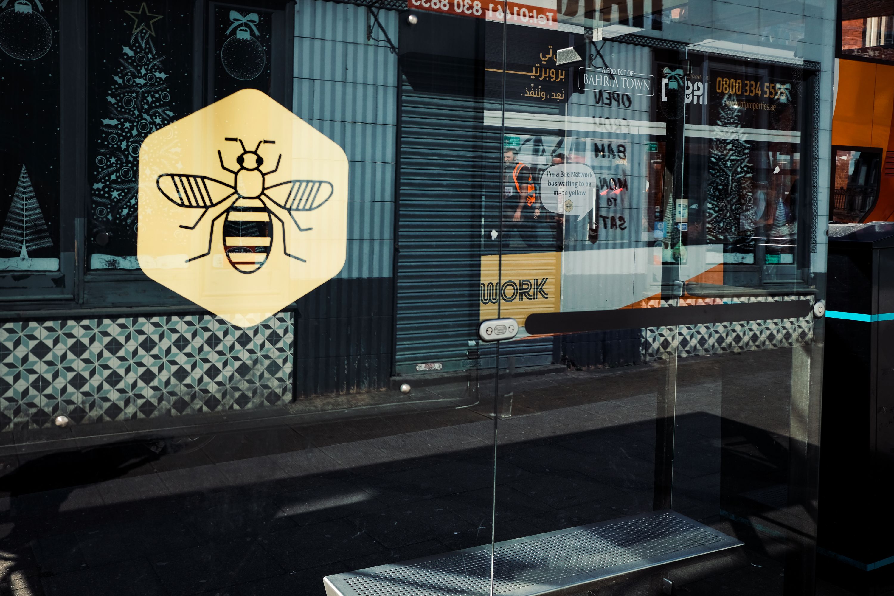 Shop window front with reflective glass and a transfer image of the Manchester Bee in yellow and black. 